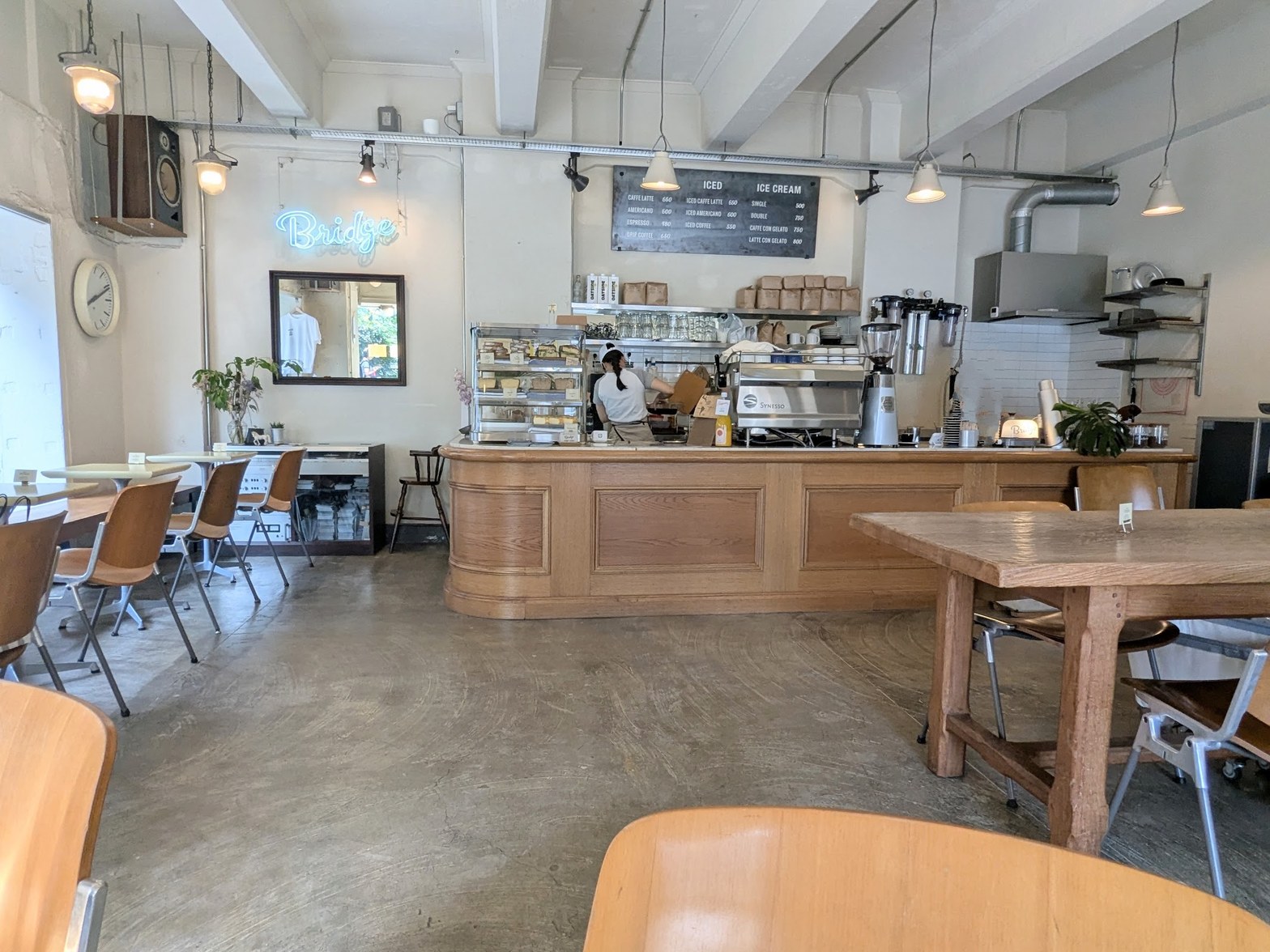 天井高のある店内にブルーのネオンサイン「Bridge」が光り、木製カウンターと丸みのあるオーク材カウンター台、コンクリート床が広がる